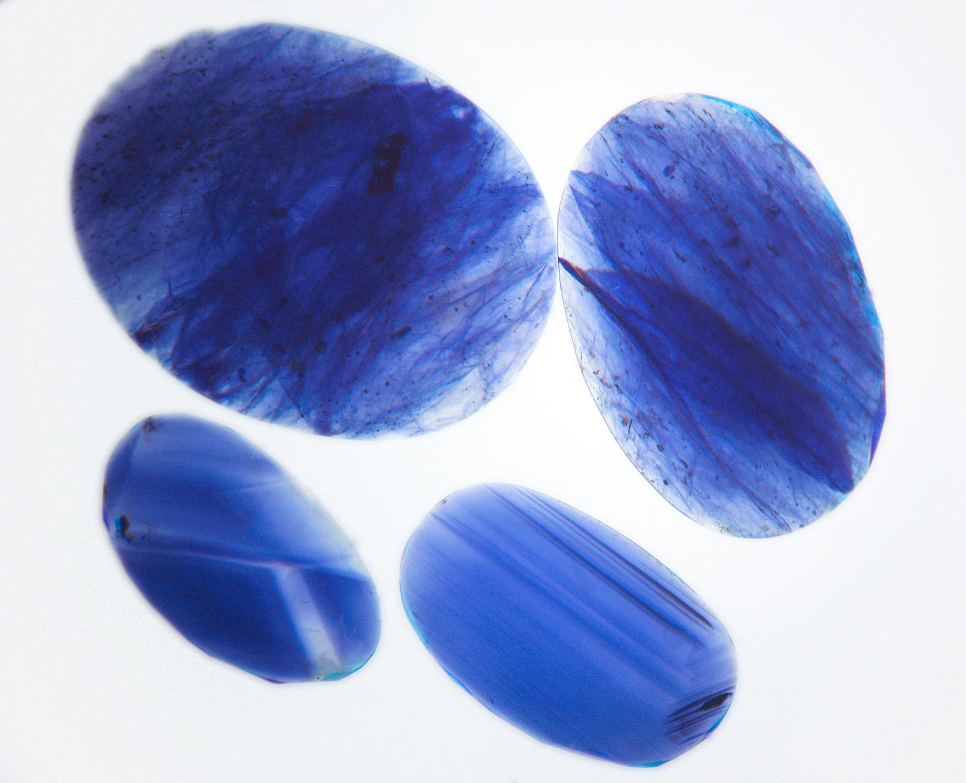 Figure 12. Immersion in di-iodomethane (methylene iodide) in diffuse light-field illumination quickly reveals the blue color concentrations in the cobalt-glass filled sapphires (top two stones), whereas natural sapphires show angular color zoning (lower two stones). Image corrected to remove yellow color of liquid. (Photo: Wimon Manorotkul, Lotus Gemology).