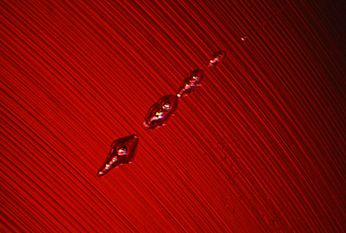 Elongated gas bubbles torpedo through curved striae within the depths of a Verneuil synthetic ruby. Photo © John I. Koivula/microWorld of Gems.