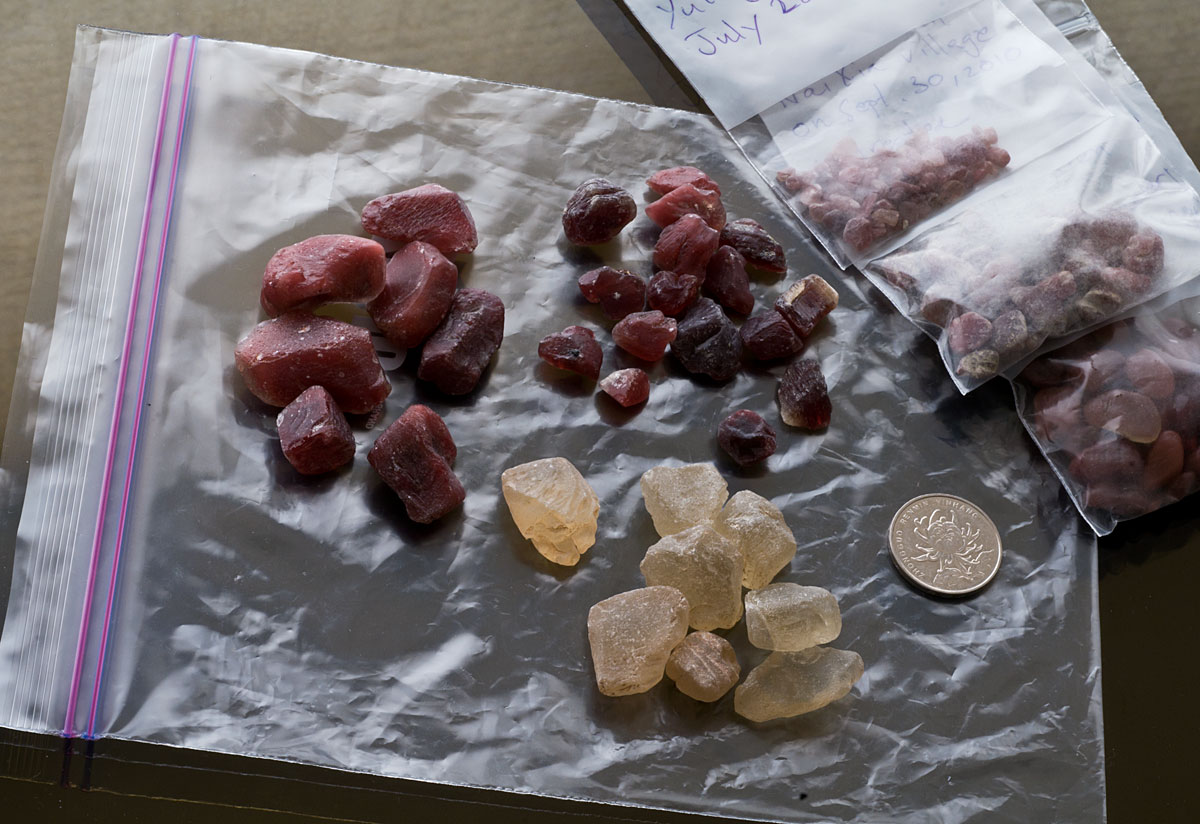 Figure 3. Pale yellow untreated andesine said to come from Inner Mongolia, flanked by two lots of deep red treated andesine. The three bags of rough on the right are natural Tibetan andesine. Untreated and treated Inner Mongolian andesines courtesy of Marco Cheung of Litto Gems. Photo: Wimon Manorotkul