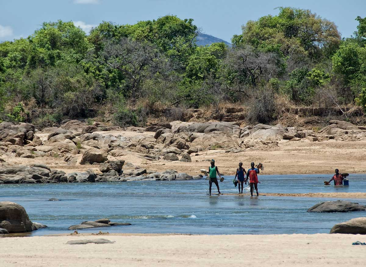 Miners fording the Ruvuma river that separates Tanzania from Mozambique, in Tanzania's Tunduru district. Gems are found on both sides of the river. Lotus Gemology.